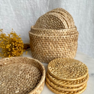 May include: Set of woven round coasters in a natural beige color. The coasters are stacked on top of each other and are made of a natural material. The coasters are in a woven pattern and have a natural, rustic look.