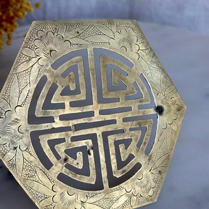 May include: A hexagonal brass ornament with a decorative floral design and a central cutout of a traditional Chinese symbol. The ornament is intricately engraved with a repeating pattern of flowers and leaves.