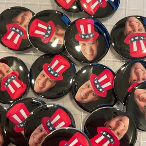 May include: A collection of round, black and white buttons with a red, white, and blue Uncle Sam hat design. Each button features a different person's face.