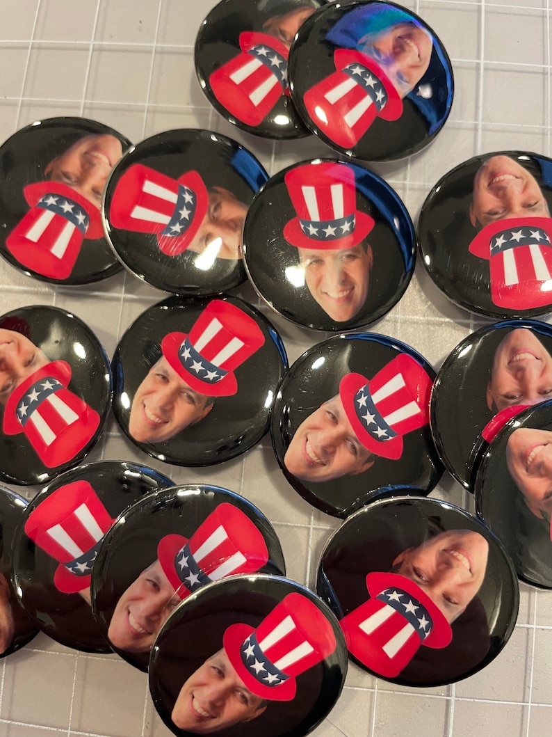 May include: A collection of round, black and white buttons with a red, white, and blue Uncle Sam hat design. Each button features a different person's face.