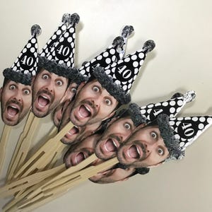 May include: A set of 8 black and white polka dot party hats with a number 40 on each hat. The hats are attached to wooden skewers and feature a printed image of a person's face.
