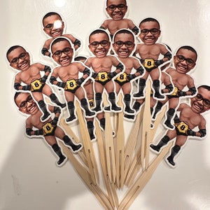 May include: A set of 12 cupcake toppers featuring cartoon images of a person wearing a wrestling belt with the number 8 on it. The toppers are printed on white cardstock and attached to wooden skewers.