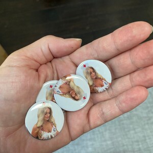 May include: Four round white buttons with a red cross in the top right corner. Each button features a photo of a woman wearing a white nurse's uniform and a stethoscope.