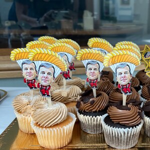May include: A collection of cupcakes decorated with cartoon character toppers. The toppers are of people wearing red jumpsuits and parachutes. The cupcakes are frosted in chocolate and vanilla.