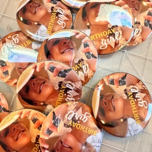 May include: A set of round, colorful buttons with a photo of a person wearing a hat and the text "Birthday girl" on each button.