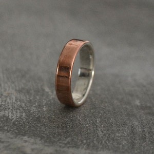 May include: A copper and silver band ring. The ring is made of two metals, with the copper on the outside and the silver on the inside.