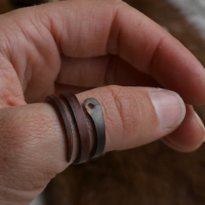 May include: A copper ring with a hammered finish and a small hole in the top. The ring is wrapped around a finger.