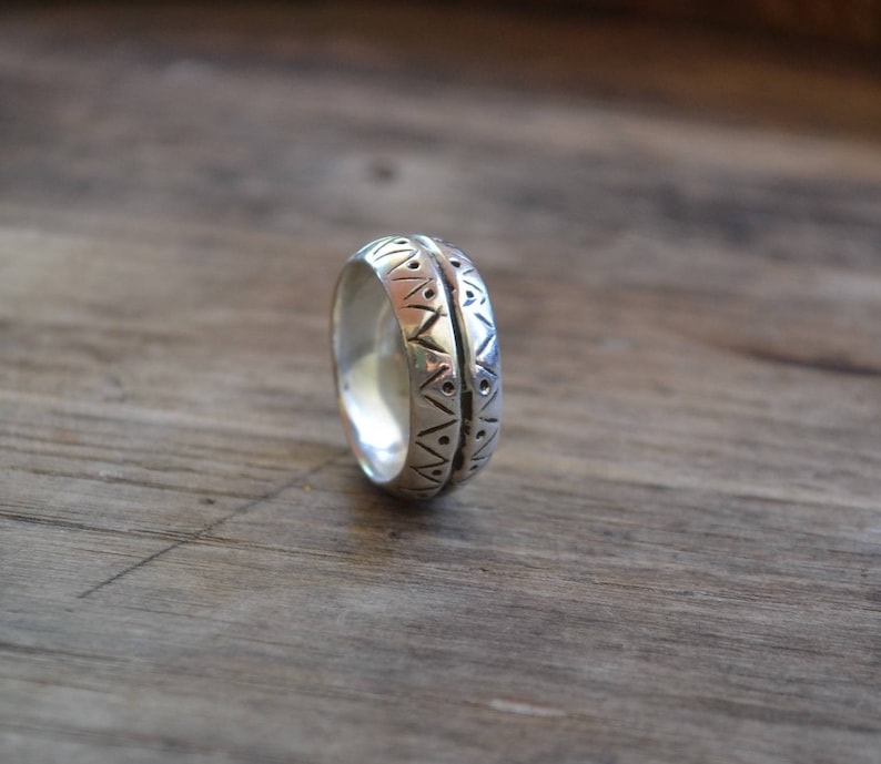 May include: A silver band ring with a geometric pattern engraved around the entire band.