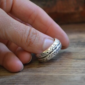 May include: A silver ring with a geometric pattern. The ring is worn on a finger.