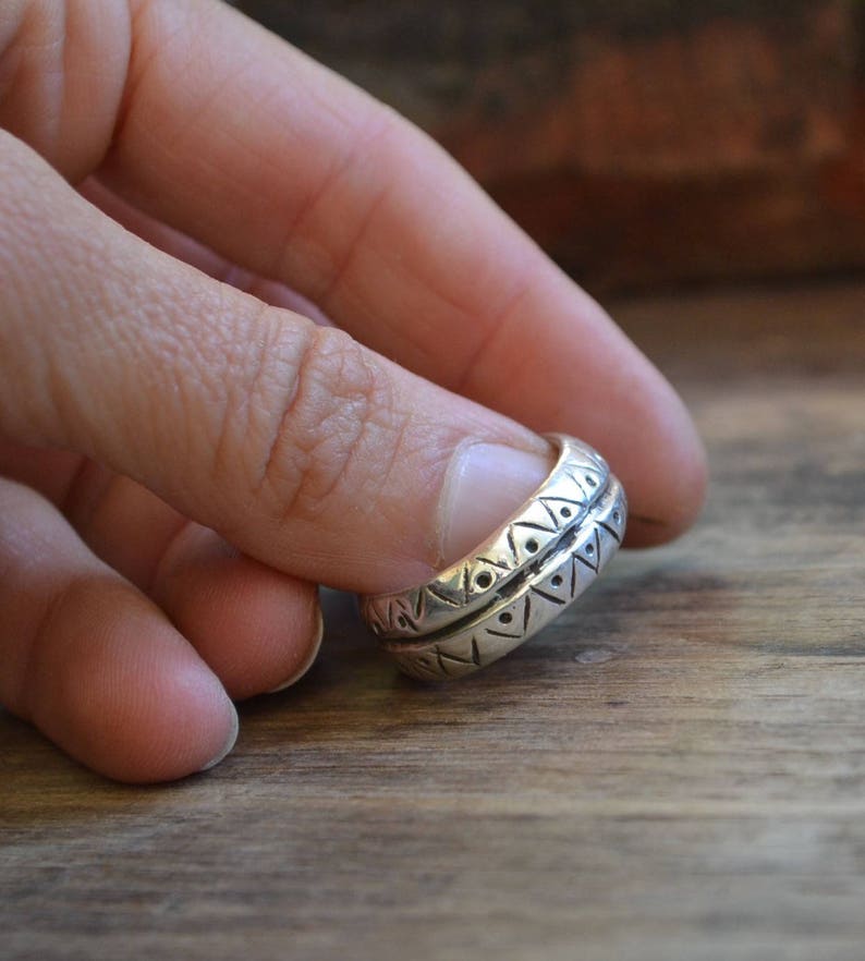 May include: A silver ring with a geometric pattern. The ring is worn on a finger.