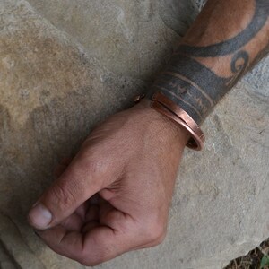 May include: A copper bracelet with a simple design. The bracelet is worn on a person's wrist.