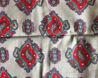 May include: Close-up of a fabric with a repeating paisley pattern. The design features large, red paisley shapes with teal and purple accents, set against a light gray background. Smaller, oval paisley motifs are also present.