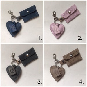 May include: Four keychains featuring a heart-shaped charm embossed with the letters MO and a small rectangular pouch with a snap closure. The set includes a dark blue, a light pink with star patterns, a dark gray, and a beige perforated pouch.
