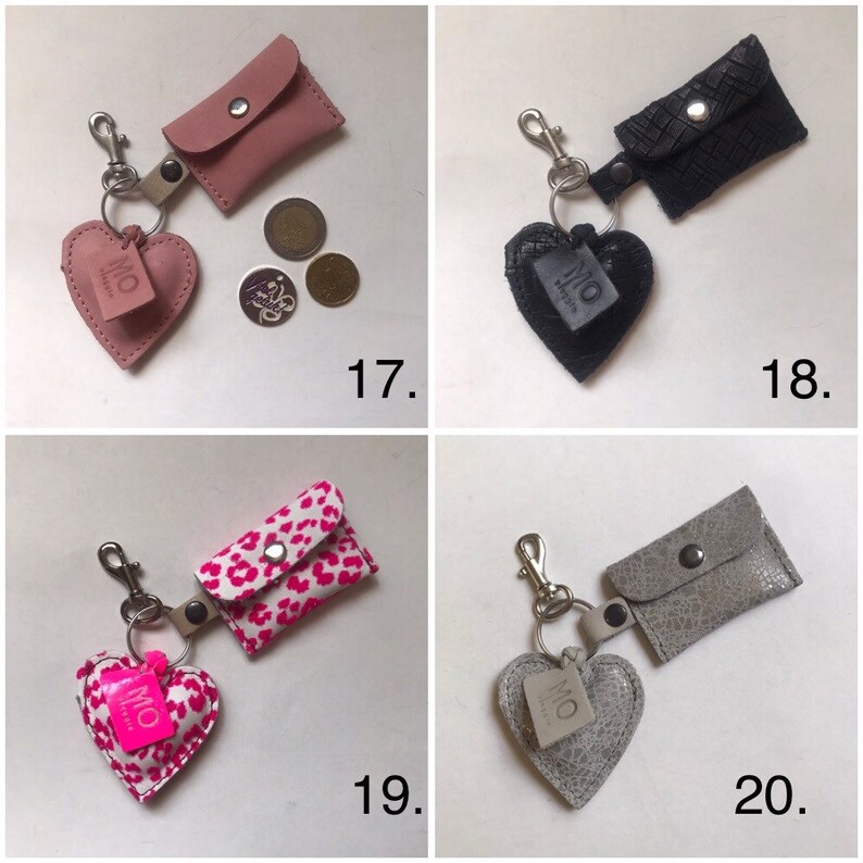 May include: Four keychains featuring a small rectangular pouch with a snap closure and a heart-shaped charm attached to a metal ring and lobster clasp. The designs include solid pink, black textured, pink leopard print, and grey metallic patterns.