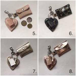 May include: Four keychains labeled 5, 6, 7, and 8, each featuring a small rectangular pouch with a snap closure and a heart-shaped charm. The pouches and hearts have varied textures and metallic or matte finishes in pink, green, gold, and bronze.