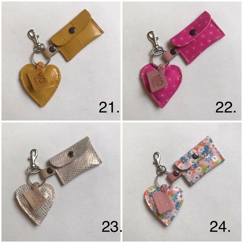 May include: Four keychains featuring a heart-shaped charm and a small rectangular pouch with a snap closure. Number 21 is mustard yellow, 22 is pink with white dots, 23 is metallic snakeskin, and 24 has a colorful floral pattern. Each has a metal clip.