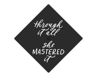 May include: Black graduation cap with white text that reads "Through it all, she mastered it."