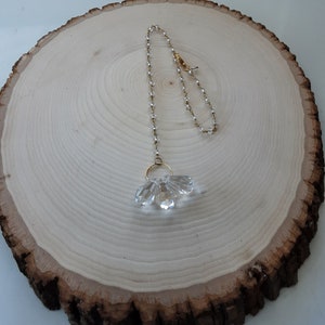 May include: A crystal chandelier prism with a gold chain and a clear crystal bead chain. The prism is hanging from a wooden surface.