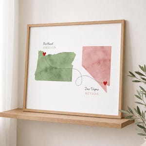 May include: A framed wall art print featuring a watercolor map of Oregon in green and Nevada in pink. A dashed black line connects the two states with a small red heart at each location. The text reads Portland Oregon and Las Vegas Nevada.