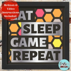 Puede incluir: Un letrero de madera enmarcado con un fondo de patrón de panal. El letrero dice "Eat Sleep Game Repeat" en letras negras con una superposición metálica plateada.