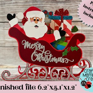 K&ouml;nnte beinhalten: Ein roter und silberner Glitzer-Weihnachtsmann in einem Schlitten mit den Worten "Frohe Weihnachten" an der Seite. Der Schlitten ist mit verpackten Geschenken gef&uuml;llt. Die fertige Datei ist 6,2 Zoll mal 5,1 Zoll mal 1,2 Zoll gro&szlig;.