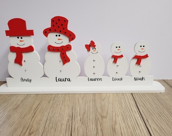 Op de afbeelding: Vijf witte houten sneeuwmanversieringen met rode hoeden en sjaals. De sneeuwmannen staan op een witte basis met de namen Andy, Laura, Lauren, Louis en Noah geschreven onder elke sneeuwman.