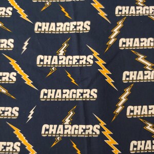 May include: Navy blue fabric with a repeating pattern of the word "CHARGERS" in white with a yellow and gold lightning bolt design. The lightning bolts are of varying sizes and orientations.