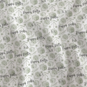 May include: A white fabric featuring a repeating pattern of sage green line-drawn roses, leaves, and sprigs. The text Kappa Delta is printed in a dark gray script font, interspersed with the Greek letters KΔ throughout the floral design.