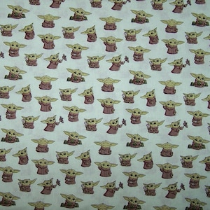Puede incluir: Tela blanca con un patrón repetido de un personaje de dibujos animados de la serie Star Wars, The Mandalorian. El personaje es verde y lleva una túnica marrón. El personaje sostiene una pequeña flor rosa.
