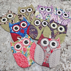 May include: Nine colorful owl-shaped pot holders with different patterns. The pot holders are made of fabric and have a quilted texture.