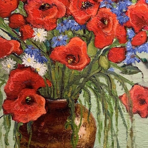 Può includere: Un mazzo di papaveri rossi e fiori blu in un vaso di ceramica marrone. Il vaso è appoggiato su una tovaglia bianca con un bordo blu.