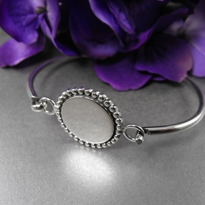 May include: A silver bangle bracelet with a round, beaded, silver charm. The charm has a smooth, white surface.