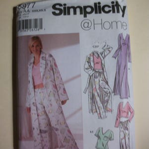 May include: Simplicity @Home sewing pattern packet. The packet features a woman wearing a pajama set, robe, and other sleepwear options. The pajama set and robe are white with a colorful print. The packet also shows illustrations of the sleepwear.