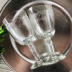 May include: Two clear glass wine glasses with etched floral designs on a silver charger.