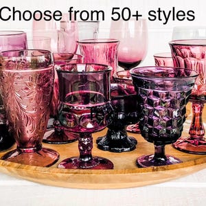 May include: A collection of various purple and pink glass goblets and tumblers with different textures and patterns, including diamond, floral, and smooth designs. The text "Choose from 50+ styles" is displayed at the top of the image.