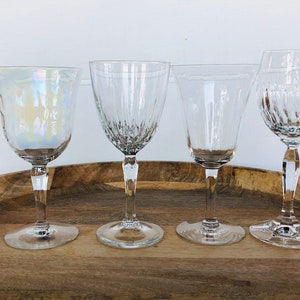May include: Four clear glass wine glasses on a wooden tray. The glass on the left has an iridescent finish.