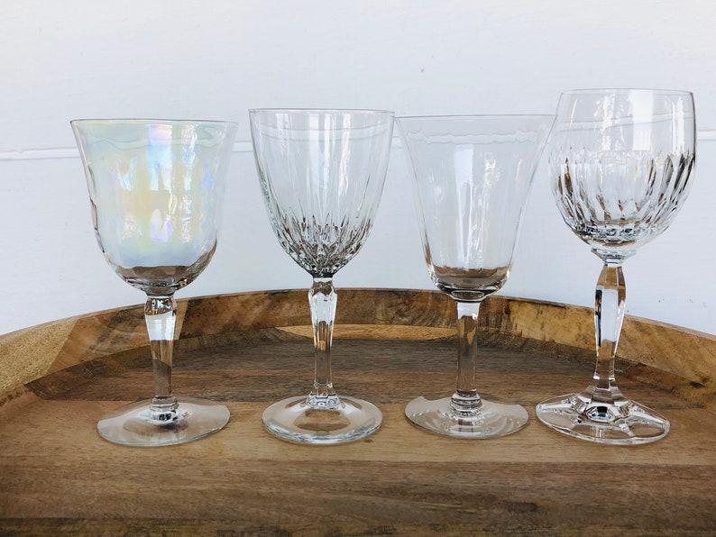 May include: Four clear glass wine glasses on a wooden tray. The glass on the left has an iridescent finish.