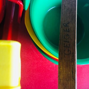 Puede incluir: Un palo de madera con la palabra "GEIGER" tallada en &eacute;l, que se encuentra sobre una pila de cuencos de pl&aacute;stico de colores. Los cuencos son verdes, amarillos y rojos.