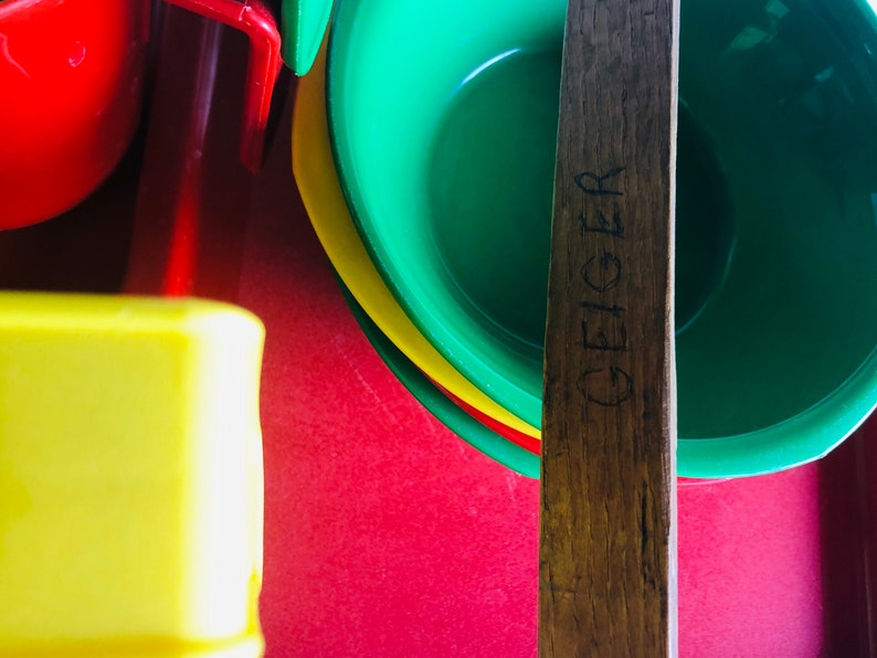 Puede incluir: Un palo de madera con la palabra "GEIGER" tallada en &eacute;l, que se encuentra sobre una pila de cuencos de pl&aacute;stico de colores. Los cuencos son verdes, amarillos y rojos.