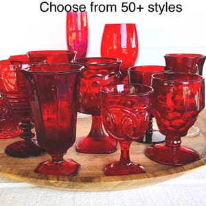 May include: A collection of various red glass goblets and drinking vessels featuring diverse textures and patterns, including faceted, ribbed, and smooth designs. The text "Choose from 50+ styles" is displayed above the red glassware.