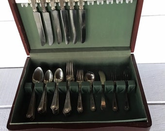 May include: A wooden box with a green velvet interior, containing a set of silverware. The silverware includes forks, knives, and spoons, all with ornate handles.