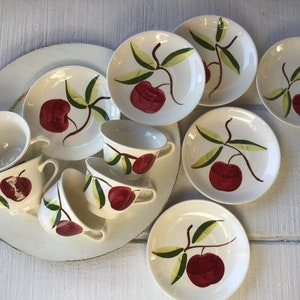 May include: A set of vintage teacups and saucers with a red apple and green leaf design. The cups and saucers are white with a glossy finish.