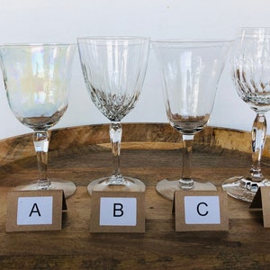 May include: Four clear glass wine glasses on a wooden tray. The glasses are labeled A, B, C, and D.