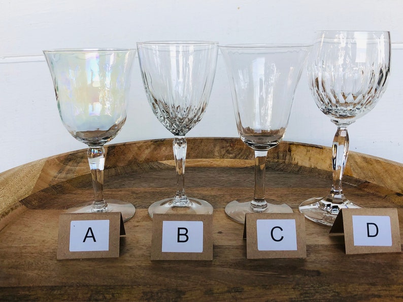May include: Four clear glass wine glasses on a wooden tray. The glasses are labeled A, B, C, and D.