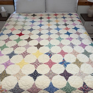 May include: A bed quilt featuring a repeating pattern of off-white circular shapes interspersed with multi-colored, patterned fabric star-shaped inserts in various hues including red, blue, yellow, green, and purple, with visible stitching.