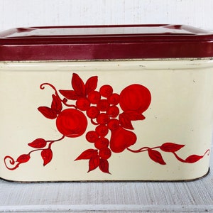 May include: Vintage white metal bread box with a red lid and a red and white fruit design. The design features apples, pears, and grapes.