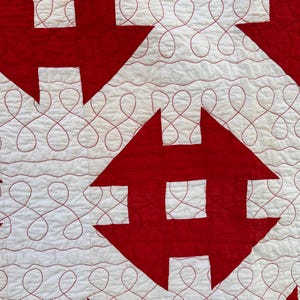 Peut inclure: Gros plan sur une courtepointe avec un motif r&eacute;p&eacute;titif de formes rouges sur fond blanc. Les formes rouges sont g&eacute;om&eacute;triques, certaines ressemblant &agrave; des croix ou des fl&egrave;ches. Les zones blanches pr&eacute;sentent des coutures rouges d&eacute;coratives.