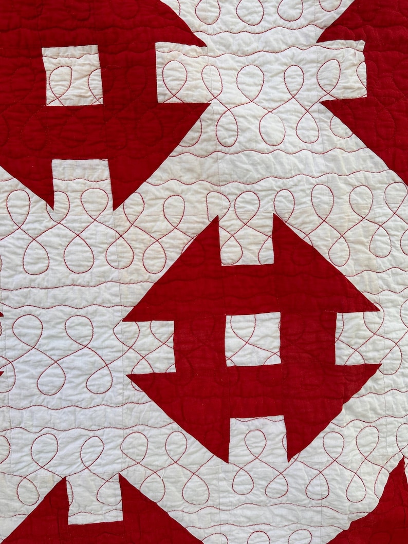 Peut inclure: Gros plan sur une courtepointe avec un motif r&eacute;p&eacute;titif de formes rouges sur fond blanc. Les formes rouges sont g&eacute;om&eacute;triques, certaines ressemblant &agrave; des croix ou des fl&egrave;ches. Les zones blanches pr&eacute;sentent des coutures rouges d&eacute;coratives.
