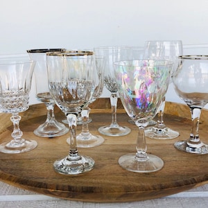 May include: A collection of seven clear glass wine glasses with silver rims on a wooden tray. The glasses are of various shapes and sizes.