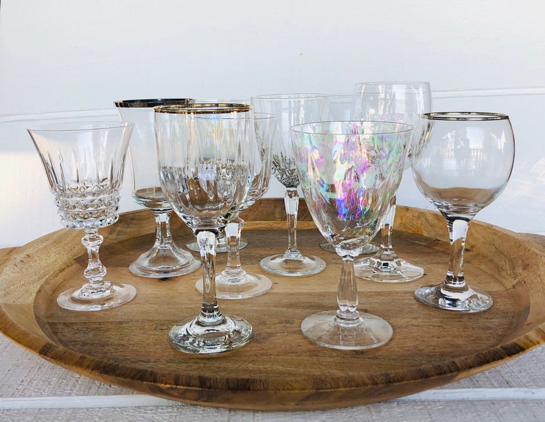 May include: A collection of seven clear glass wine glasses with silver rims on a wooden tray. The glasses are of various shapes and sizes.